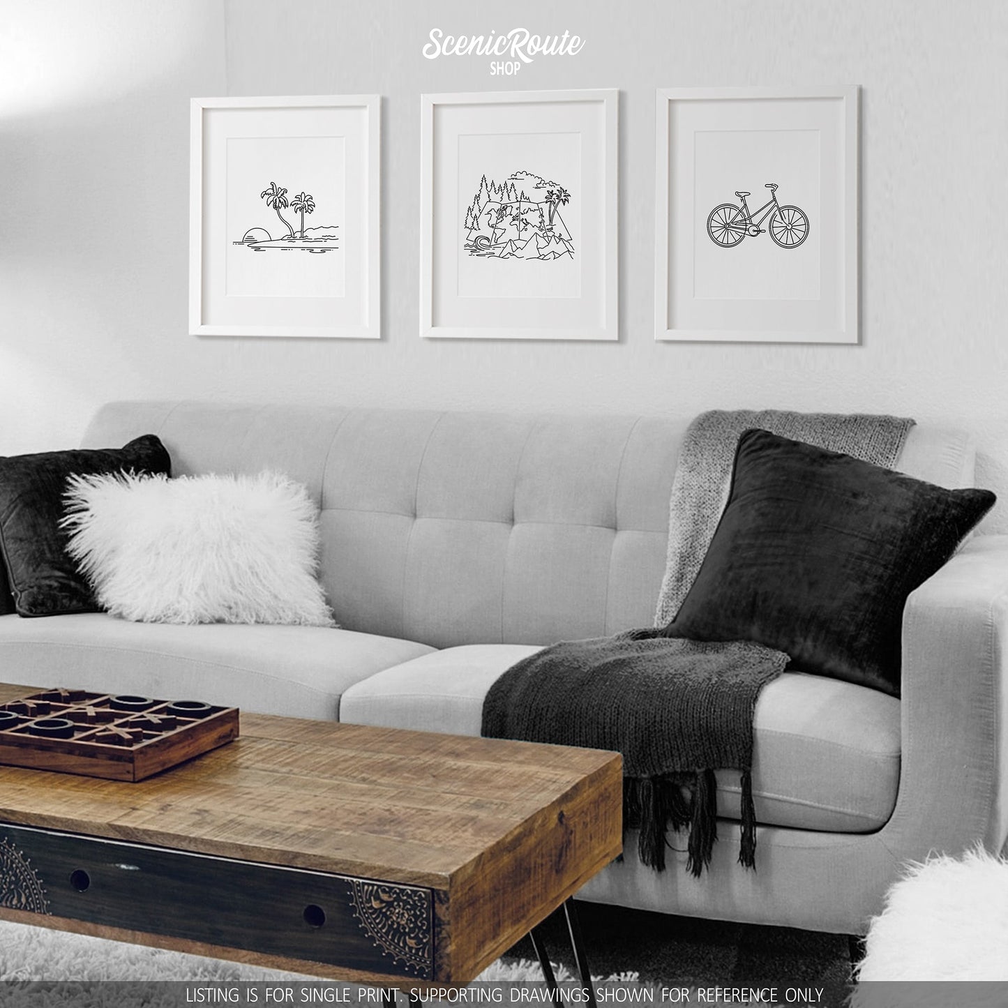 A group of three framed drawings on a wall hanging above a couch with pillows and a blanket. The line art drawings include an Island, the Adventure Map Drawing, and a Bicycle