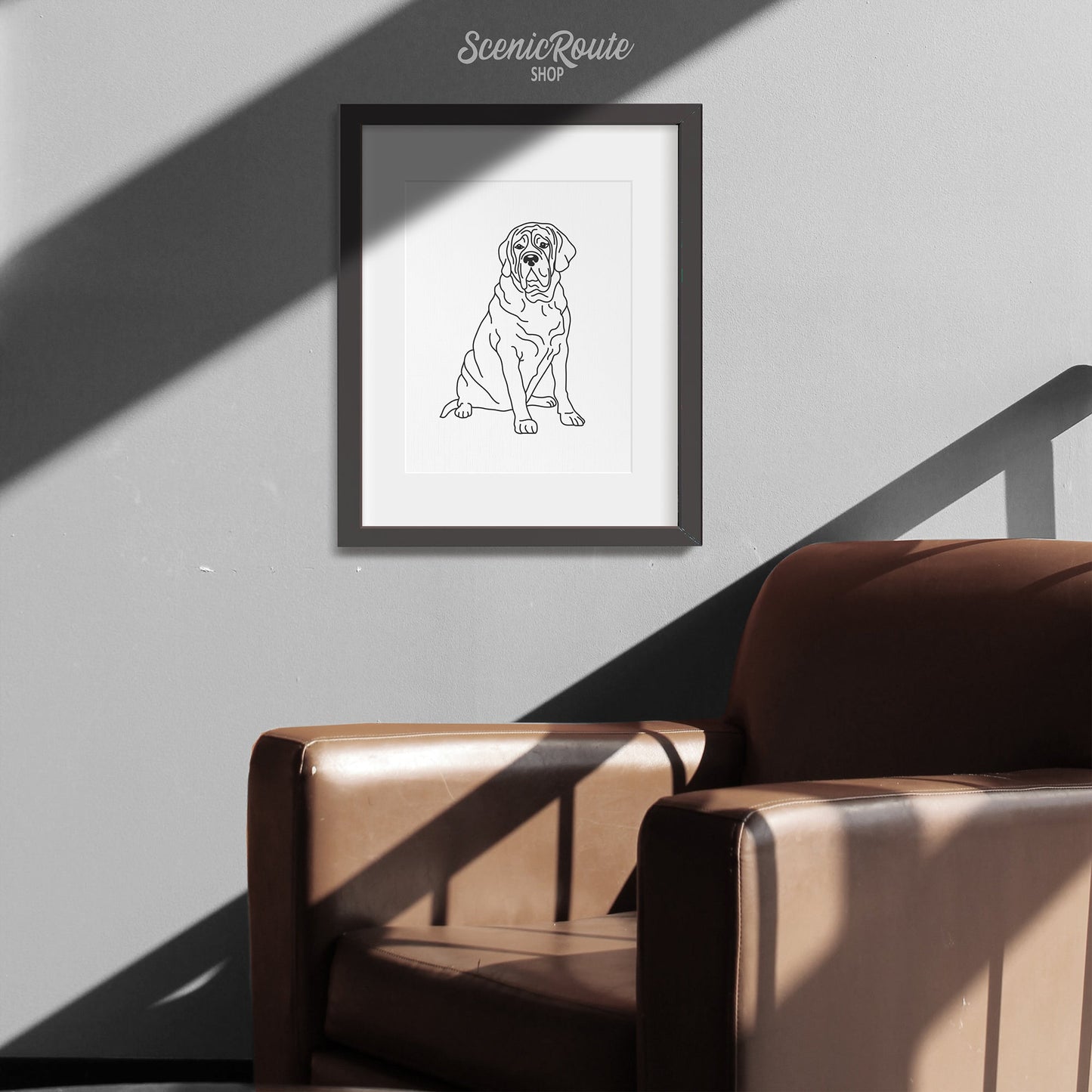 A framed line art drawing of a Mastiff dog on a white wall above a leather chair