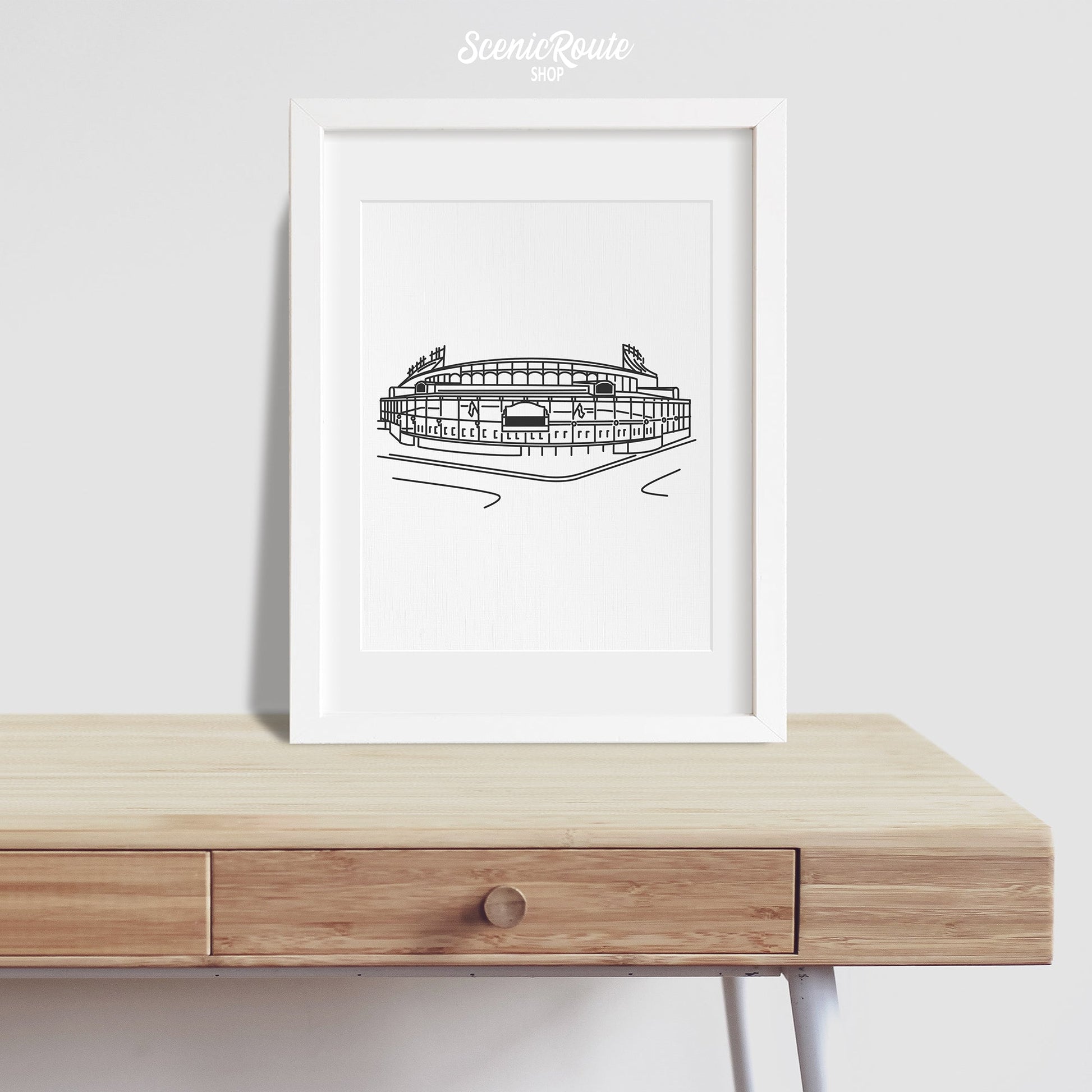 A framed line art drawing of Wrigley Field on a desk