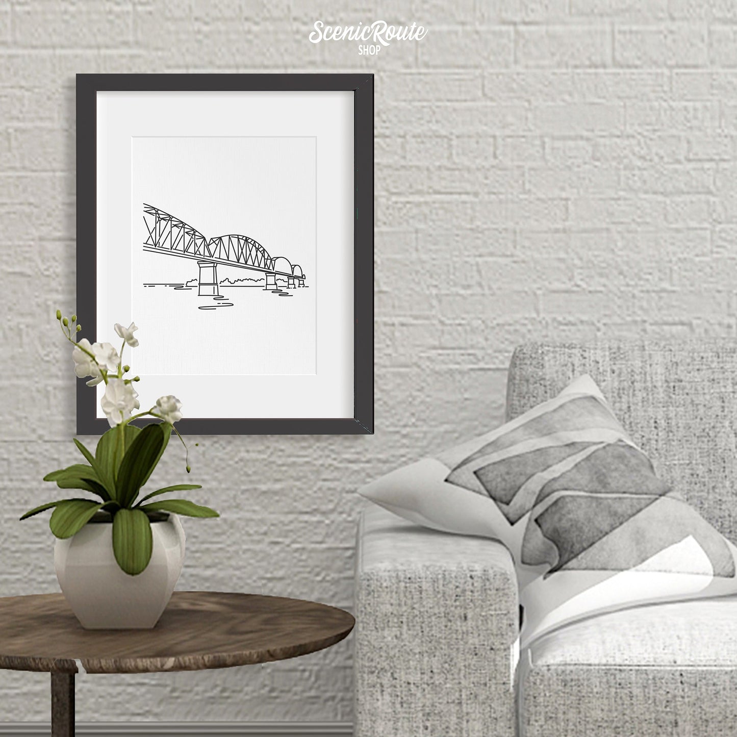 A framed line art drawing of the Big Four Bridge above a side table with a plant