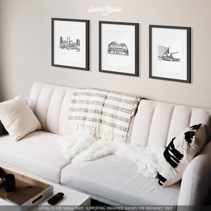 A group of three framed drawings on a white wall hanging above a couch with pillows and a blanket. The line art drawings include the Milwaukee Skyline, Brewers Stadium, and Milwaukee Art Museum