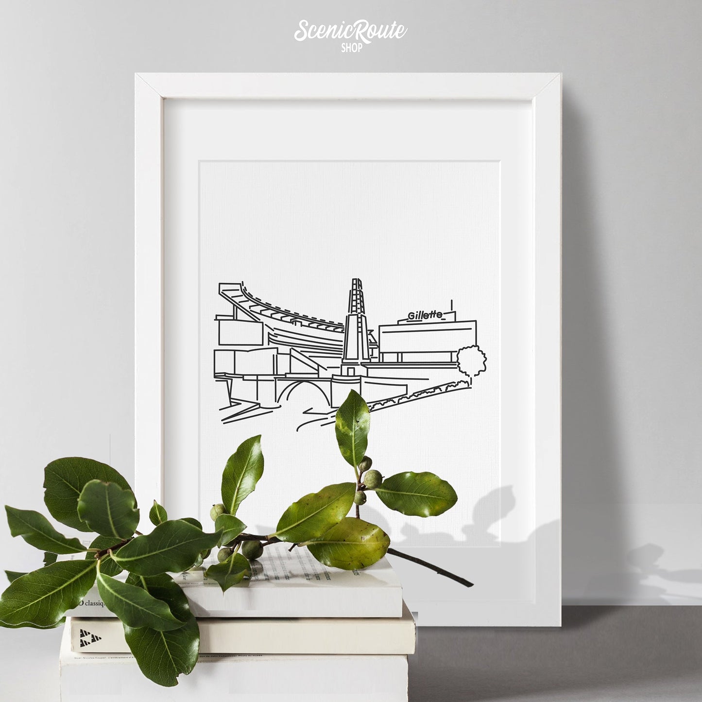 A framed line art drawing of the Patriots Stadium with books and a holly sprig