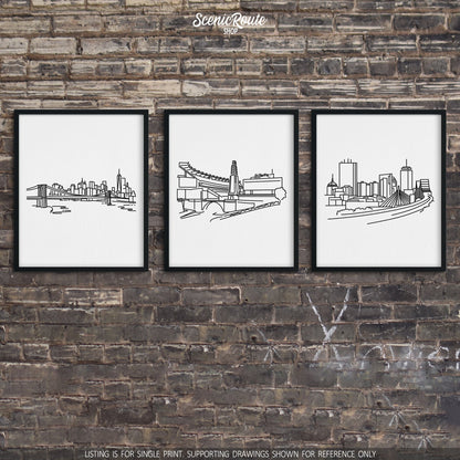 A group of three framed drawings on a brick wall. The line art drawings include the New York Skyline, Patriots Stadium, and Boston Skyline