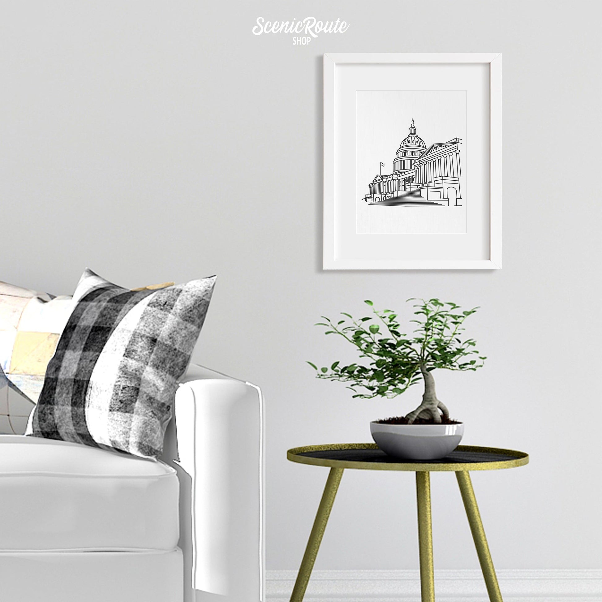 A framed line art drawing of the Capitol above a side table with a plant