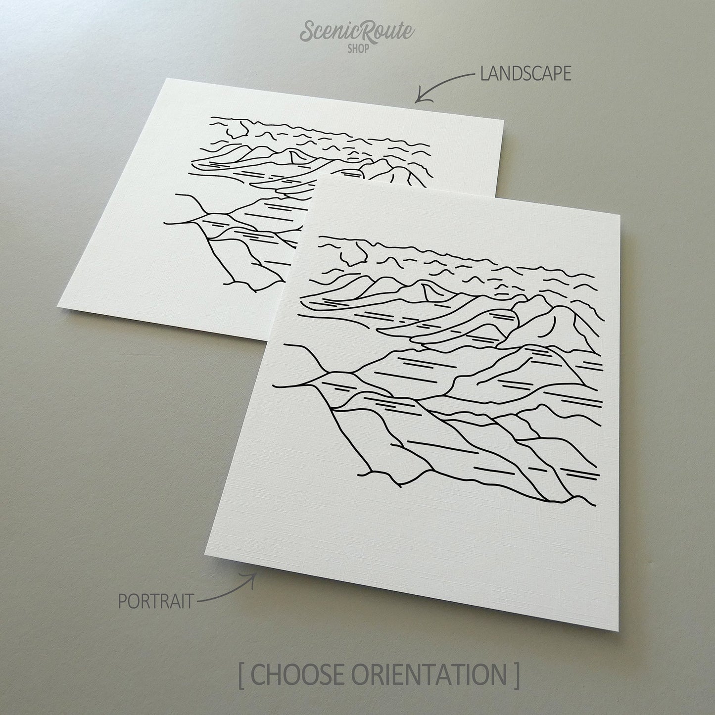 Two line art drawings of Badlands National Park on white linen paper with a gray background.  The pieces are shown in portrait and landscape orientation for the available art print options.