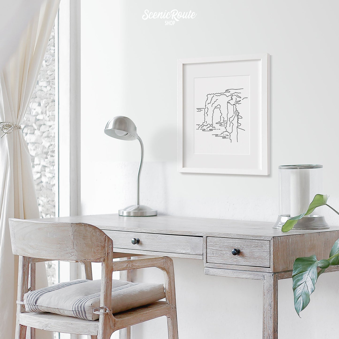 A framed line art drawing of Hawaii Volcanoes National Park hanging above a desk with a lamp