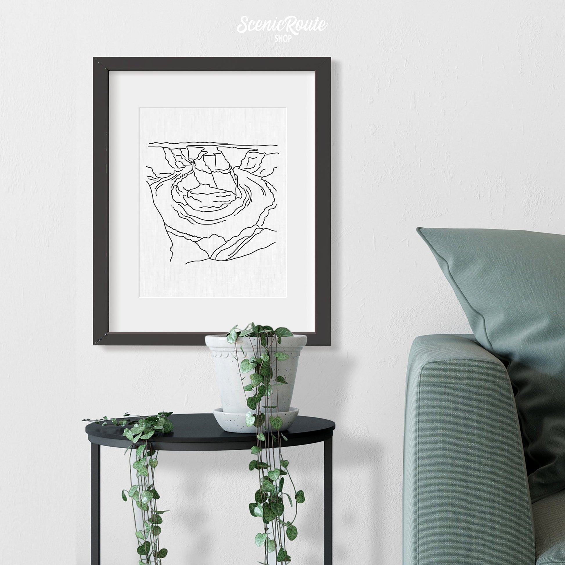 A framed line art drawing of Horseshoe Bend hanging above a side table with a plant