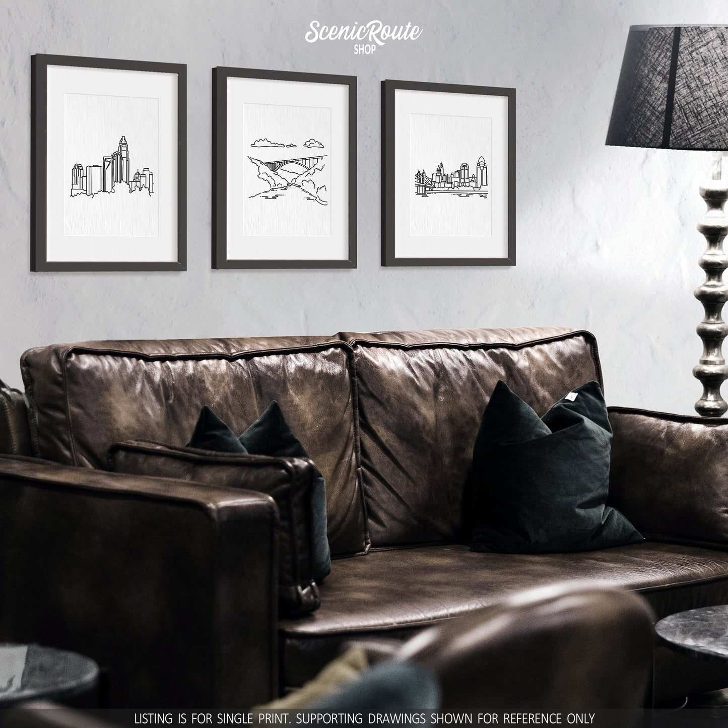 A group of three framed drawings on a wall above a couch. The line art drawings include the Charlotte Skyline, New River Gorge National Park, and Cincinnati Skyline