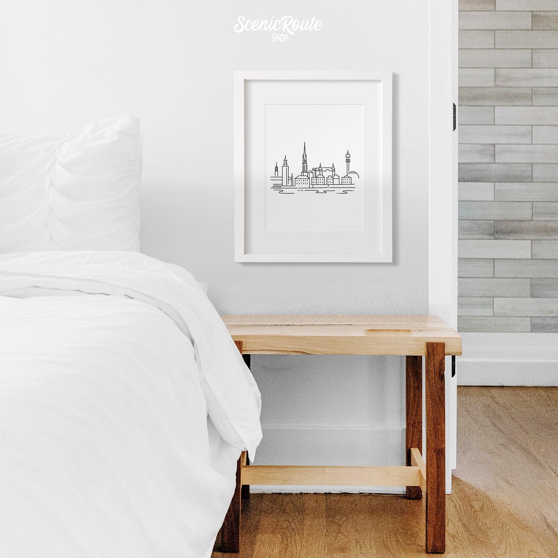 A framed line art drawing of the Stockholm Skyline above a nightstand next to a bed