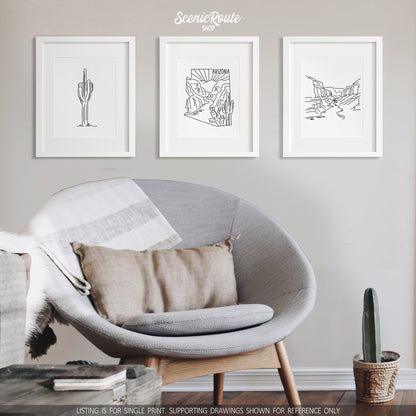 A group of three framed drawings on a white wall hanging above a round chair. The line art drawings include  a Saguaro Cactus, the Arizona State Outline, and Grand Canyon National Park